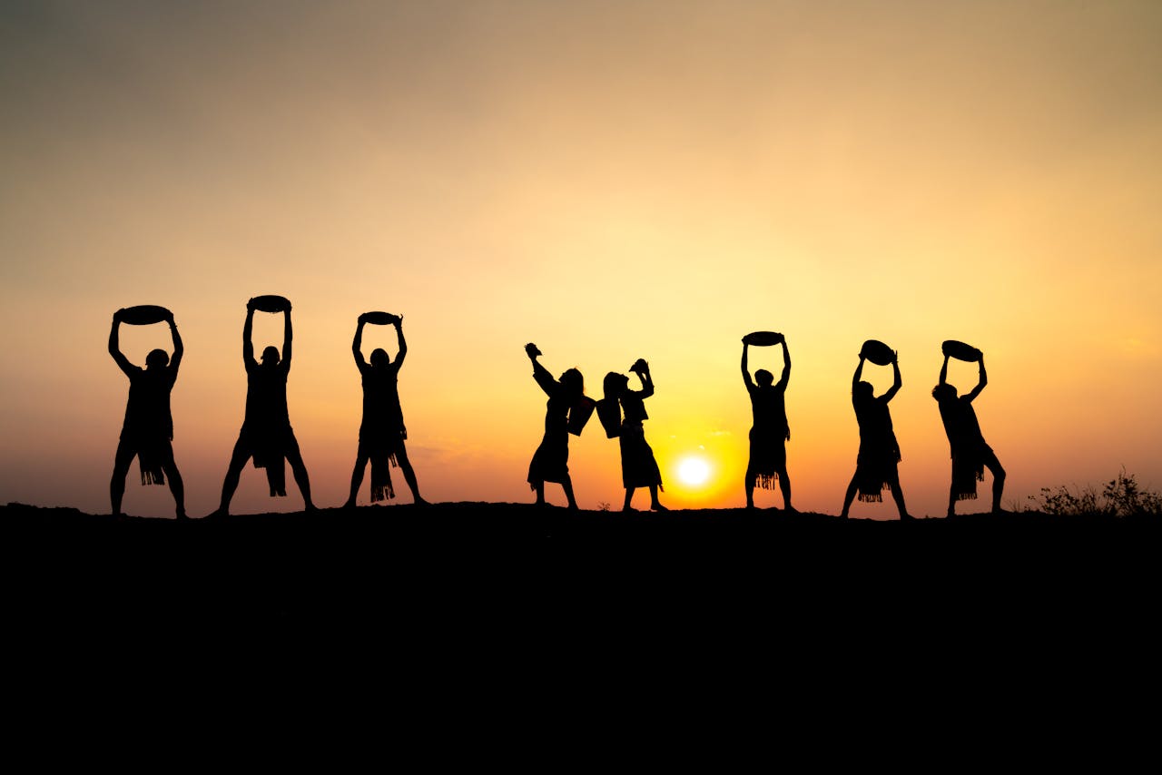 services-08 Silhouette of seven people performing traditional dance against a stunning sunset backdrop.
