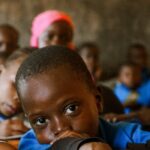 A child in a classroom looks thoughtfully, surrounded by peers in a learning environment.