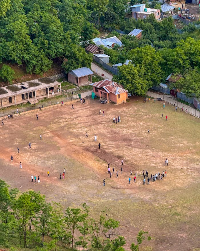 A captivating aerial shot of a group of people playing and socializing on a rural sports field surrounded by greenery.