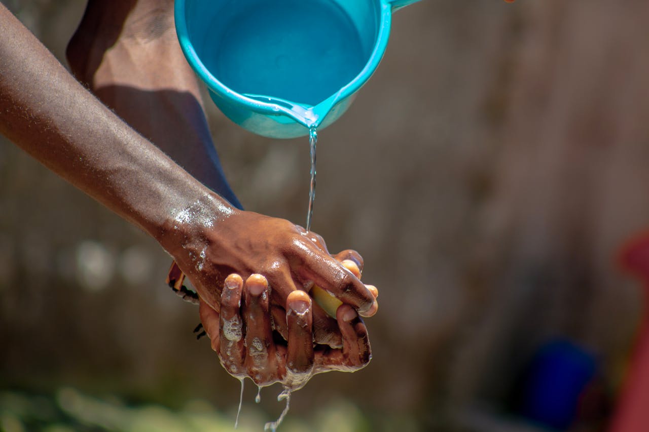 A close-up of hands being washed outdoors with flowing water and soap, promoting hygiene.